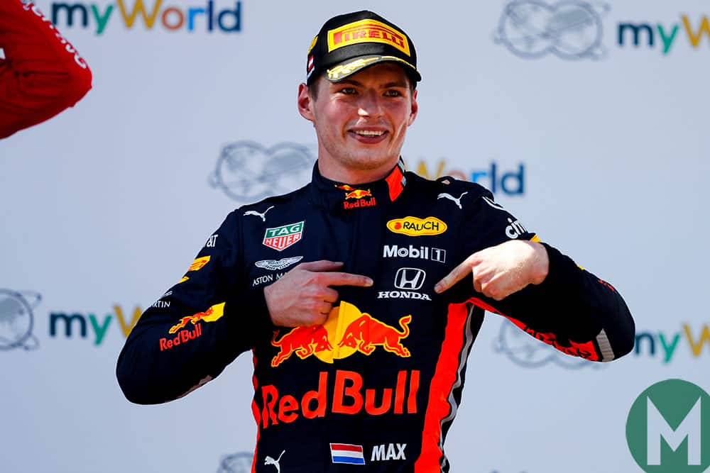 Max Verstappen points to the Honda logo on his overalls after winning the 2019 Austrian Grand Prix