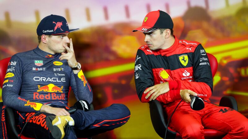 Max Verstappen holds his fingers in a v shape as he and Charles Leclerc grimace