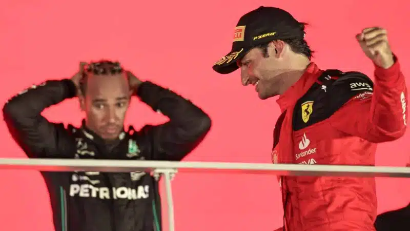 Carlos Sainz smiles on the podium after winning 2023 Singapore GP with Lewis Hamilton in background