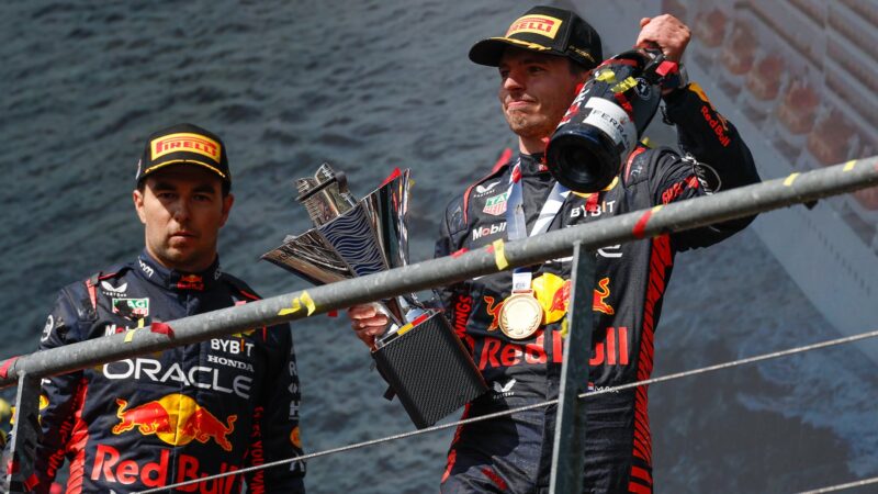 Max Verstappen holds champagne and trophy on F1 podium next to a sombre Sergio Perez after 2023 Belgian GP