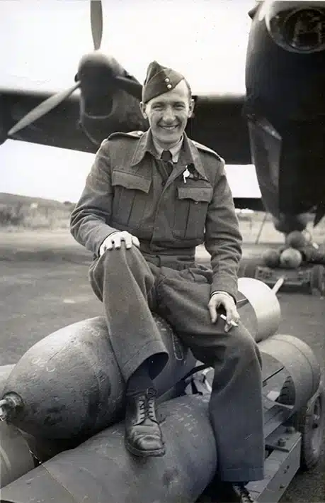Les Graham sits smoking on a stack of bombs in front of his World War 2 Lancaster