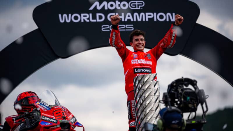 Marc Marquez holds arms in the air next to MotoGP world championship trophy after winning 2025 title