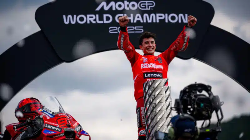 Marc Marquez holds arms in the air next to MotoGP world championship trophy after winning 2025 title